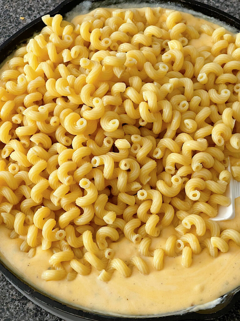 Cellentani pasta added to cheese sauce in a skillet.