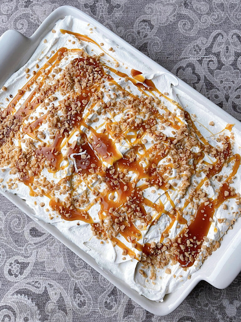 A chocolate toffee poke cake topped with toffee bits, Cool Whip, and caramel sauce.