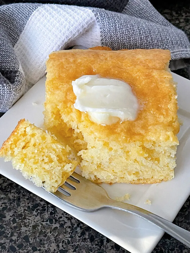 A slice of cornbread cake recipe made with a cake mix and cornbread mix topped with butter.