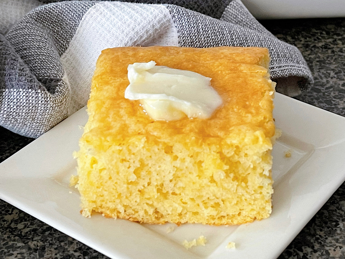 A slice of cornbread cake recipe made with a cake mix and cornbread mix topped with butter.