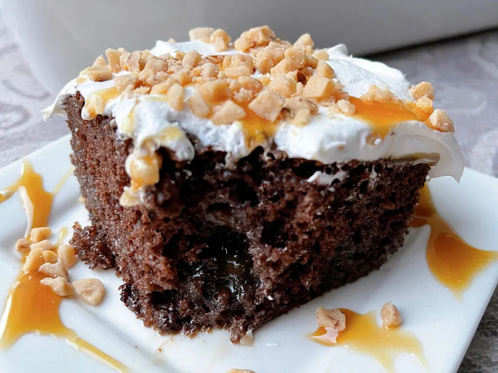 A slice of chocolate poke cake topped with Cool Whip and toffee bits.