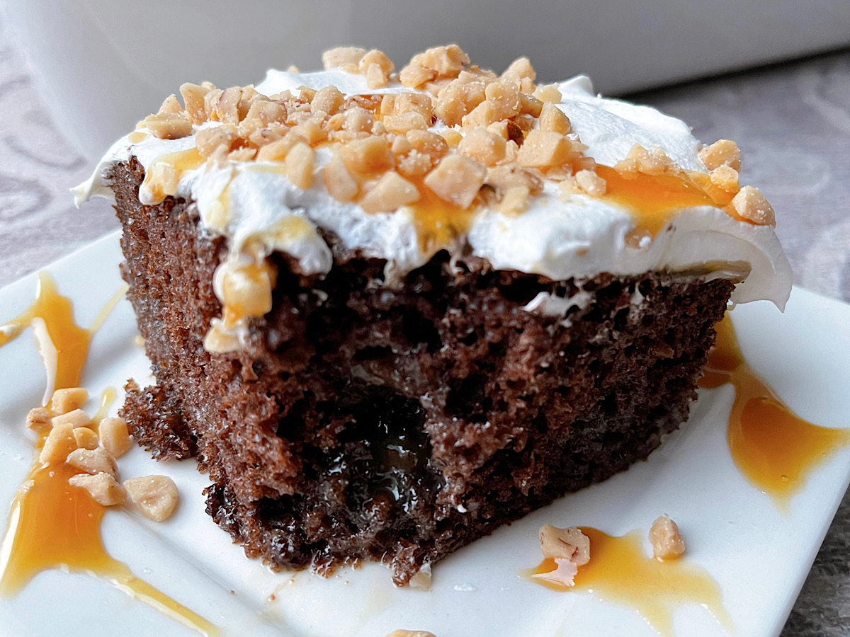 A slice of chocolate poke cake topped with Cool Whip and toffee bits.