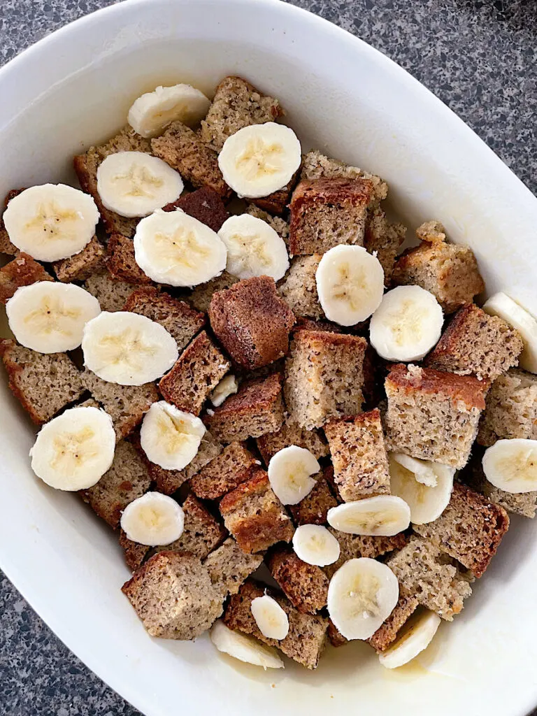 Cubes of banana bread and banana slices in a casserole dish.