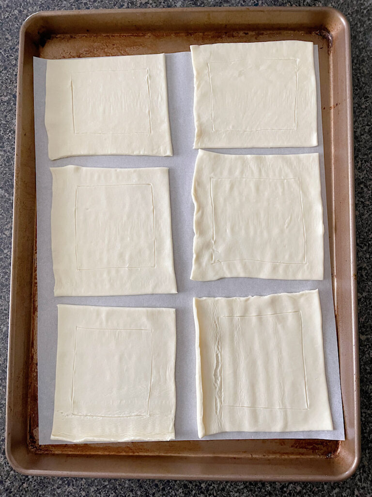A sheet of puff pastry cut into six squares with a smaller square scored in the middle.