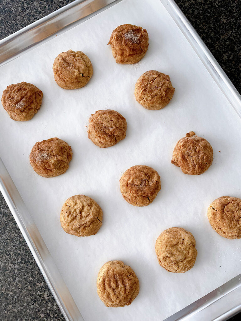 Pumpkin snickerdoodles on a parchment paper-lined baking sheet.