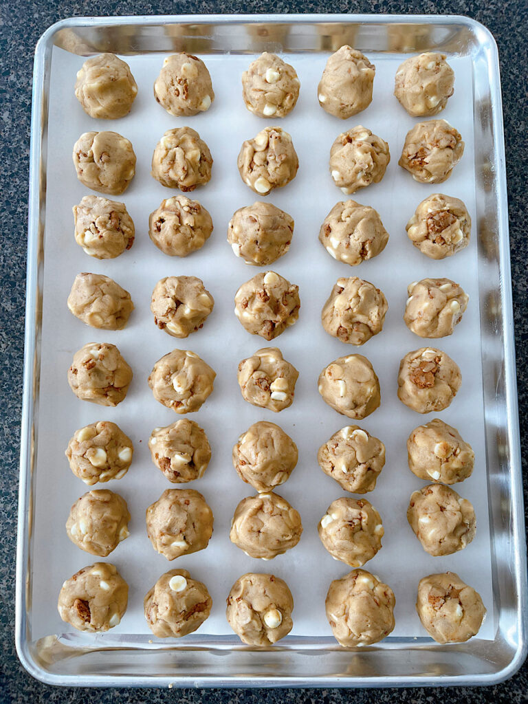Balls of cookie butter cookie dough on a baking sheet.