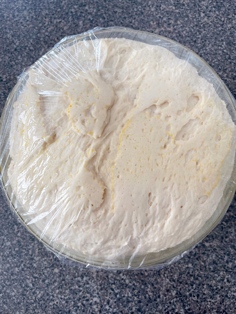 Sweet roll dough that has risen in a mixing bowl covered with plastic wrap.