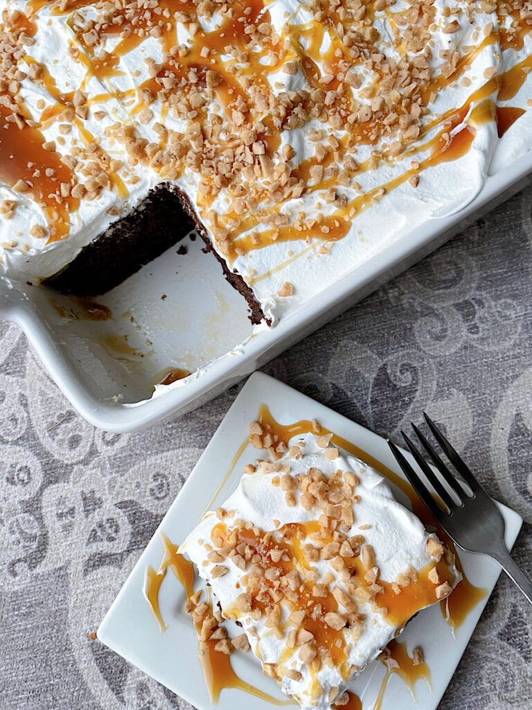 A slice of chocolate poke cake next to a cake pan missing one piece.