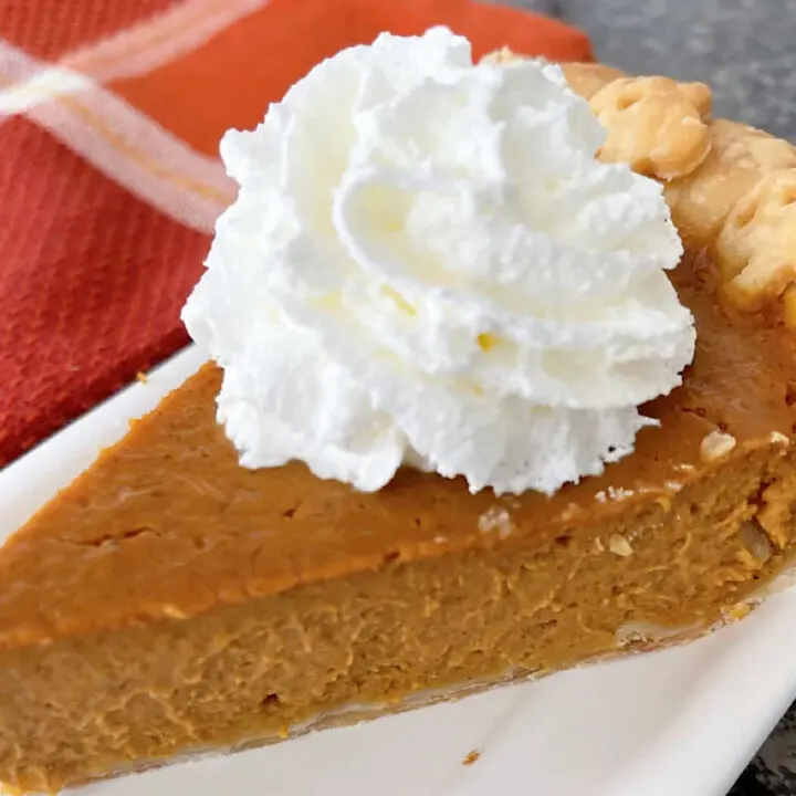A slice of copycat Costco pumpkin pie topped with whipped cream.