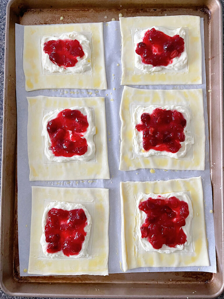 Cheesecake filling and cranberry sauce in the center of puff pastry dough squares.