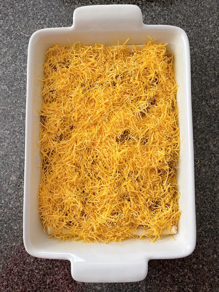 Crescent roll dough in a baking dish topped with shredded cheese and sausage.