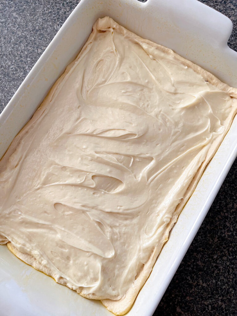 Cream cheese filling spread over a layer of crescent roll dough in a baking dish.