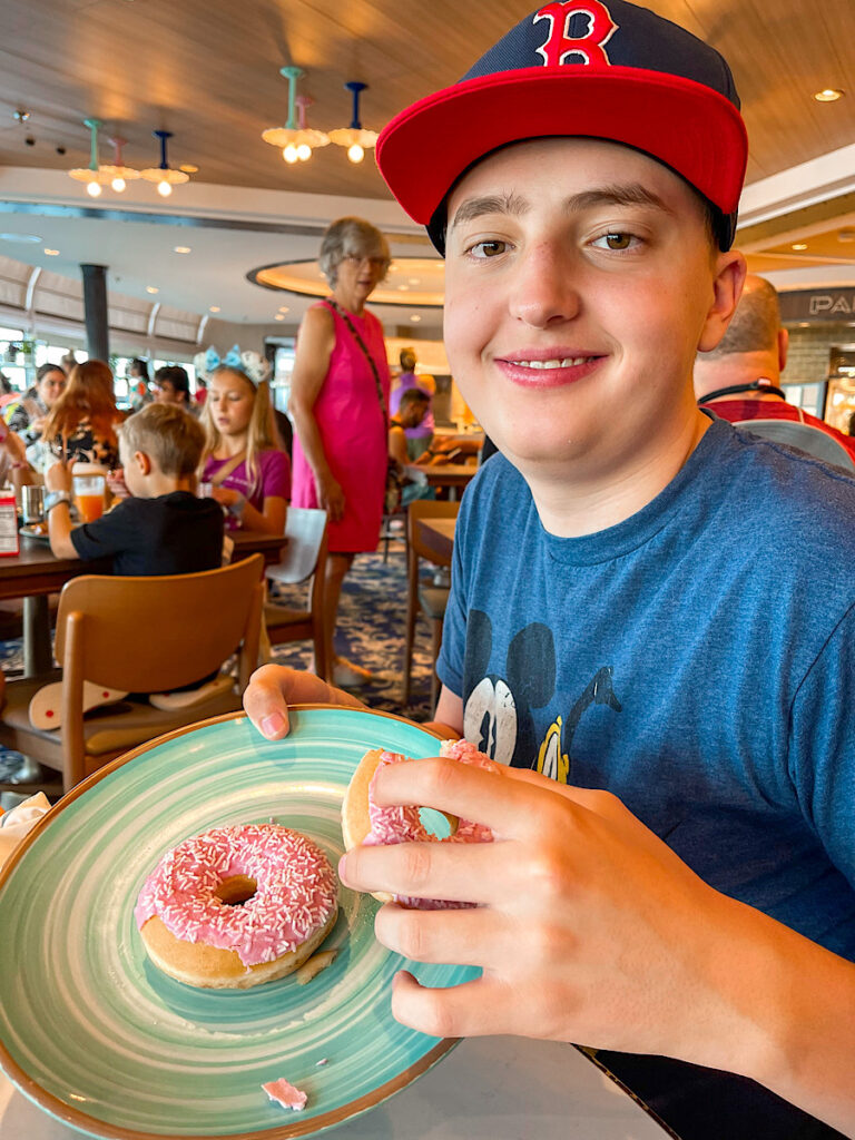 A teenager with a pink dounut from Marceline Market on the Disney Wish.