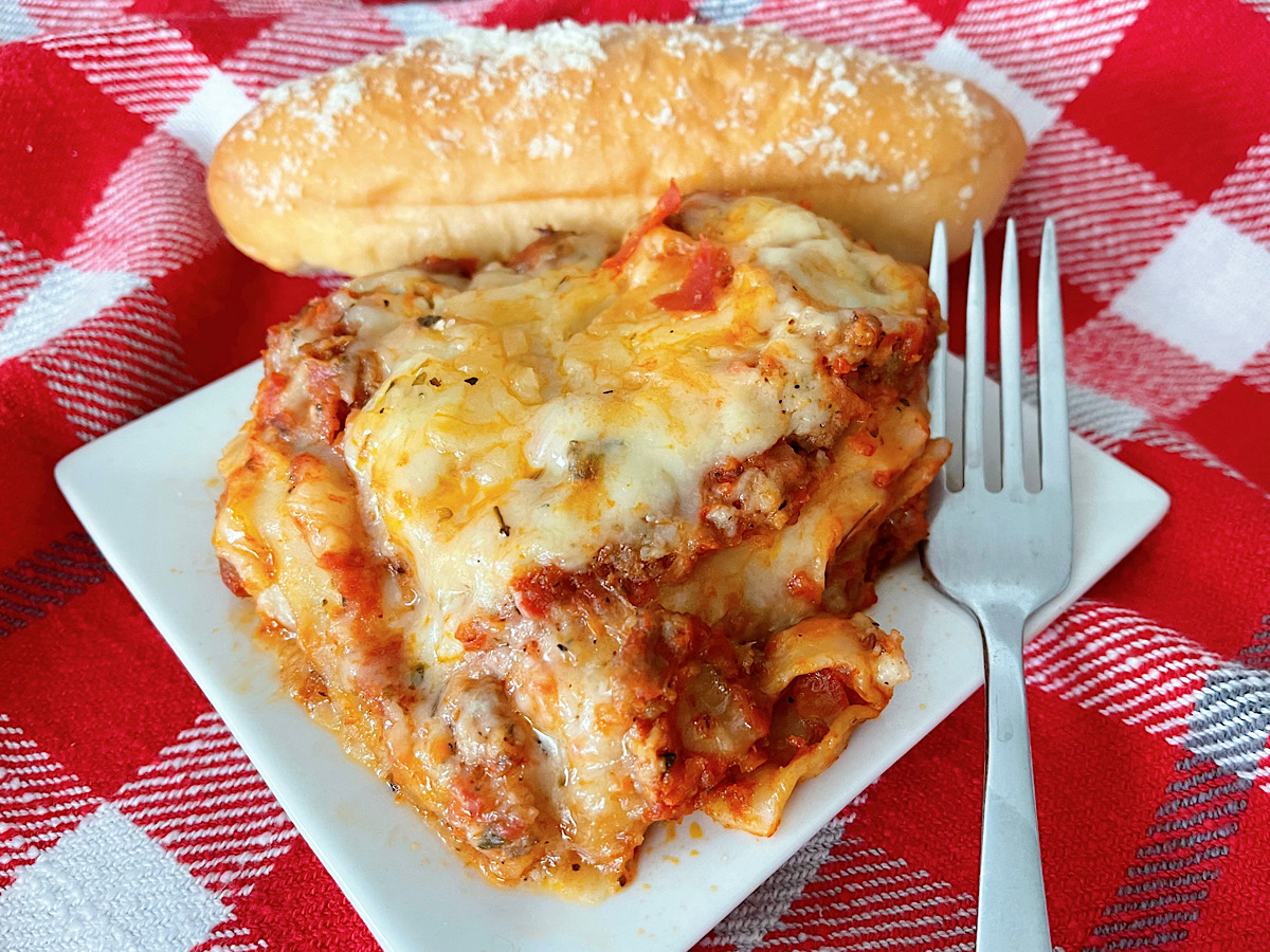 A slice of Bechamel Lasagna with a breadstick.