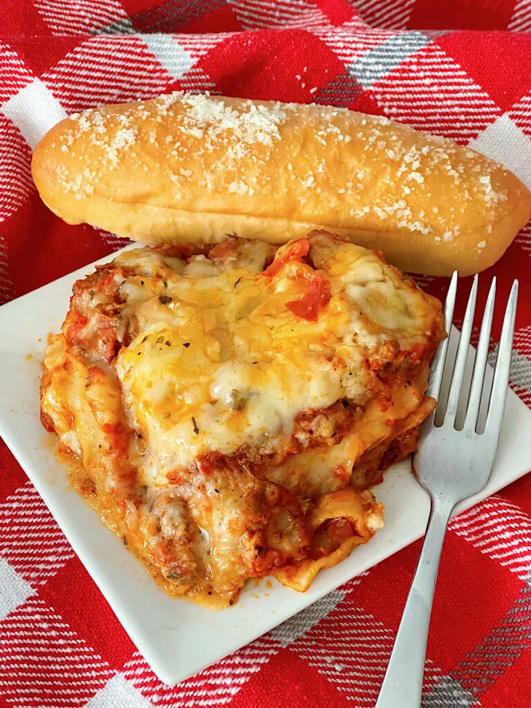 A slice of Bechamel Lasagna with a breadstick.