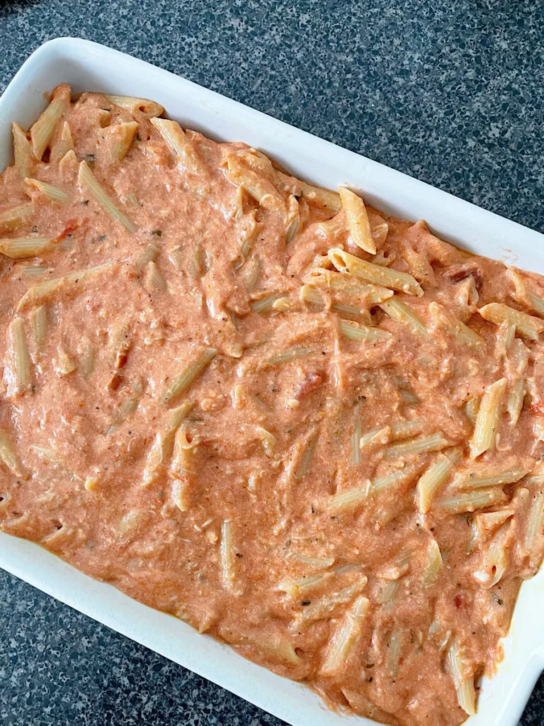 Penne pasta mixed with 5 cheese pasta sauce in a baking dish.