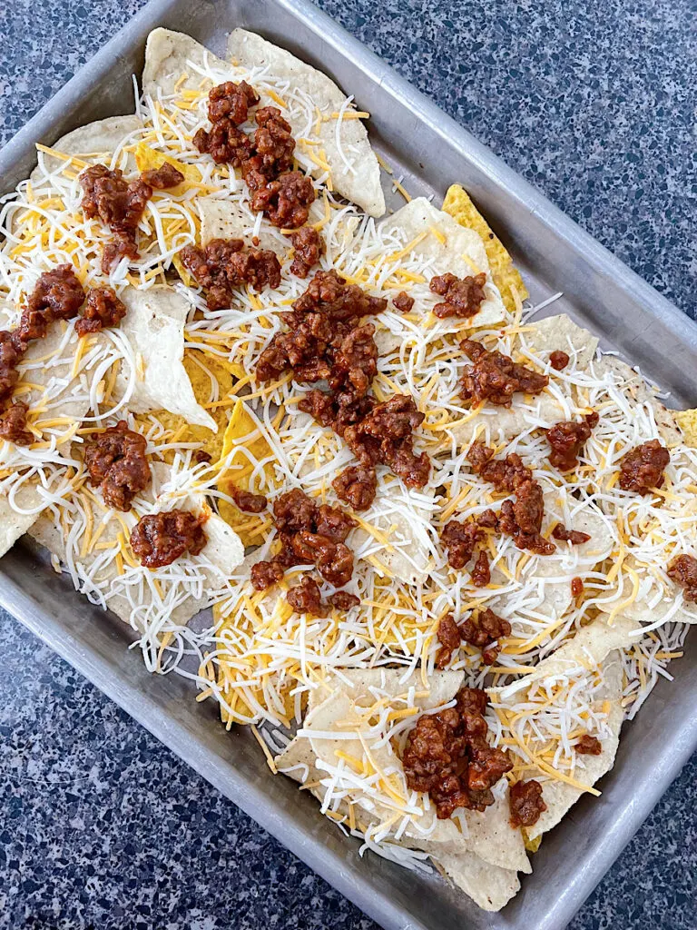 Tortilla chips on a baking sheet with ground beef and cheese.