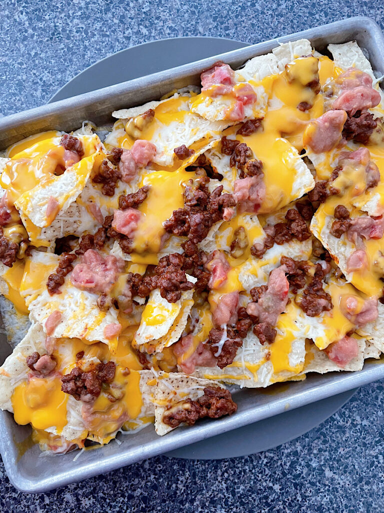 Nachos on a sheet pan with beans, ground beef, and cheese.