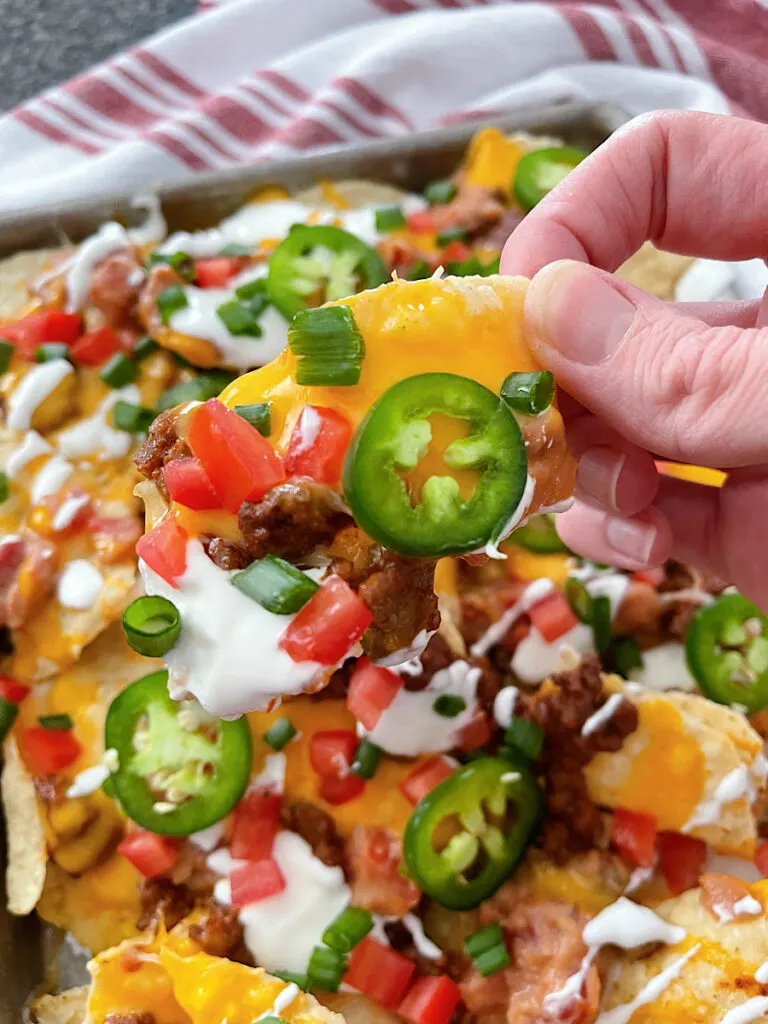 A hand holding sheet pan nachos with ground beef.