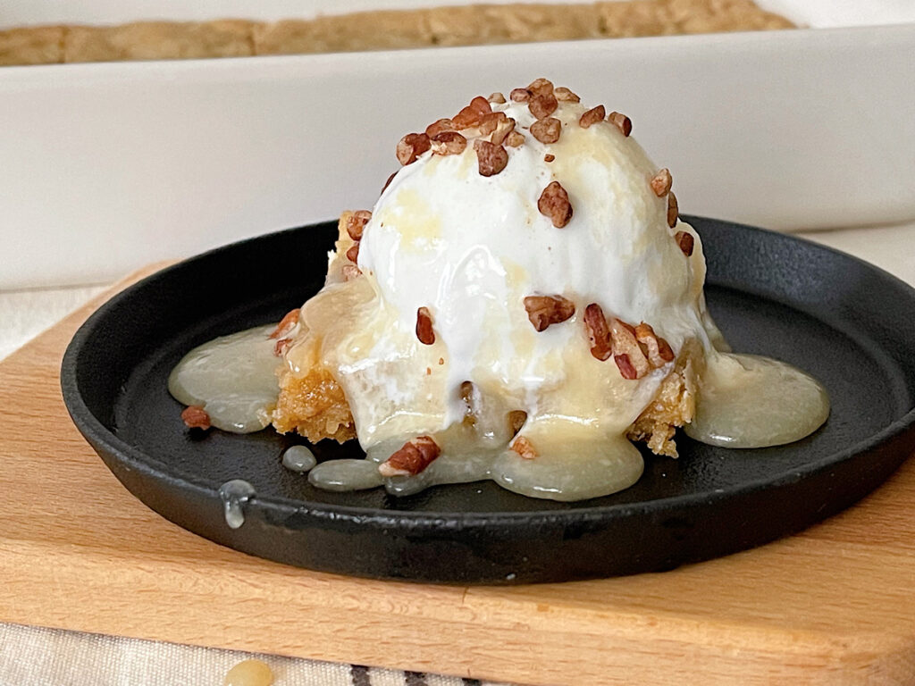A copycat Applebee's blondie topped with vanilla ice cream, maple cream sauce, and chopped pecans.