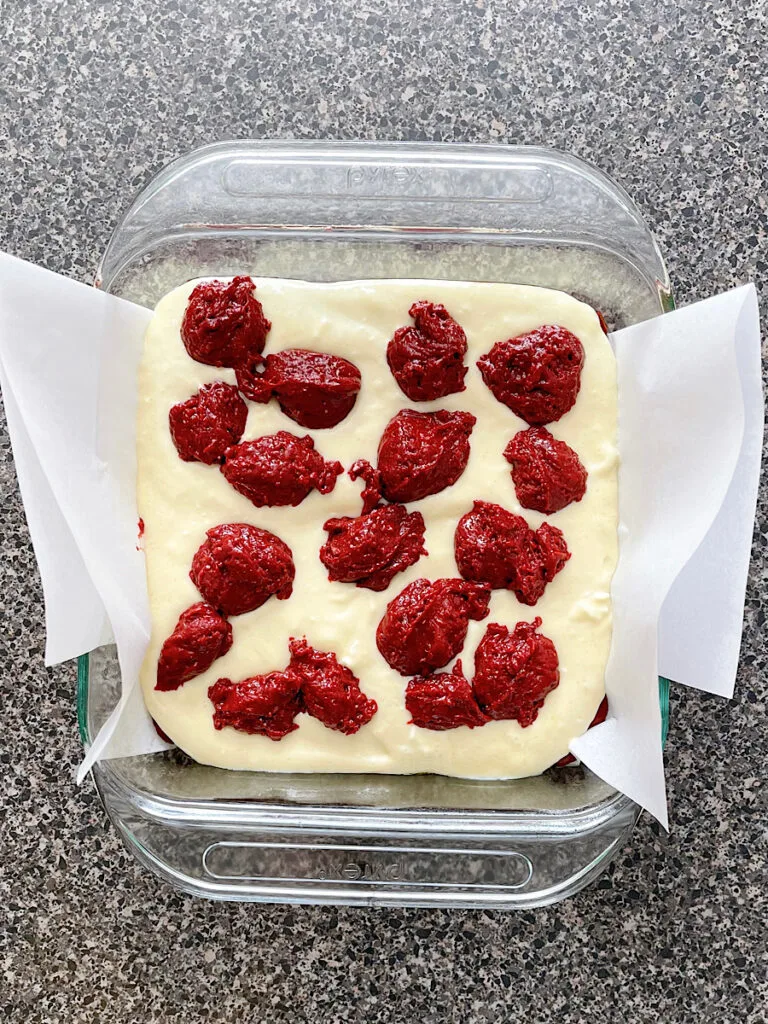 Red velvet brownie batter and cheesecake batter in a baking dish.