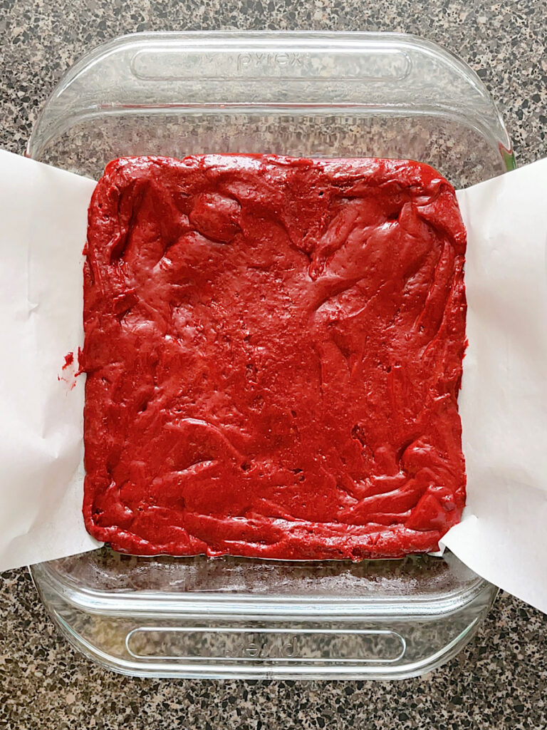 Red velvet brownie batter in a baking dish lined with parchment paper.