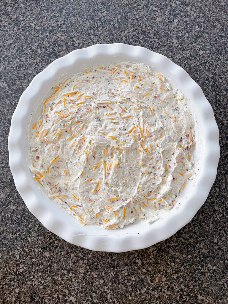 Cream cheese, shredded cheese, ranch, and bacon in a baking dish.