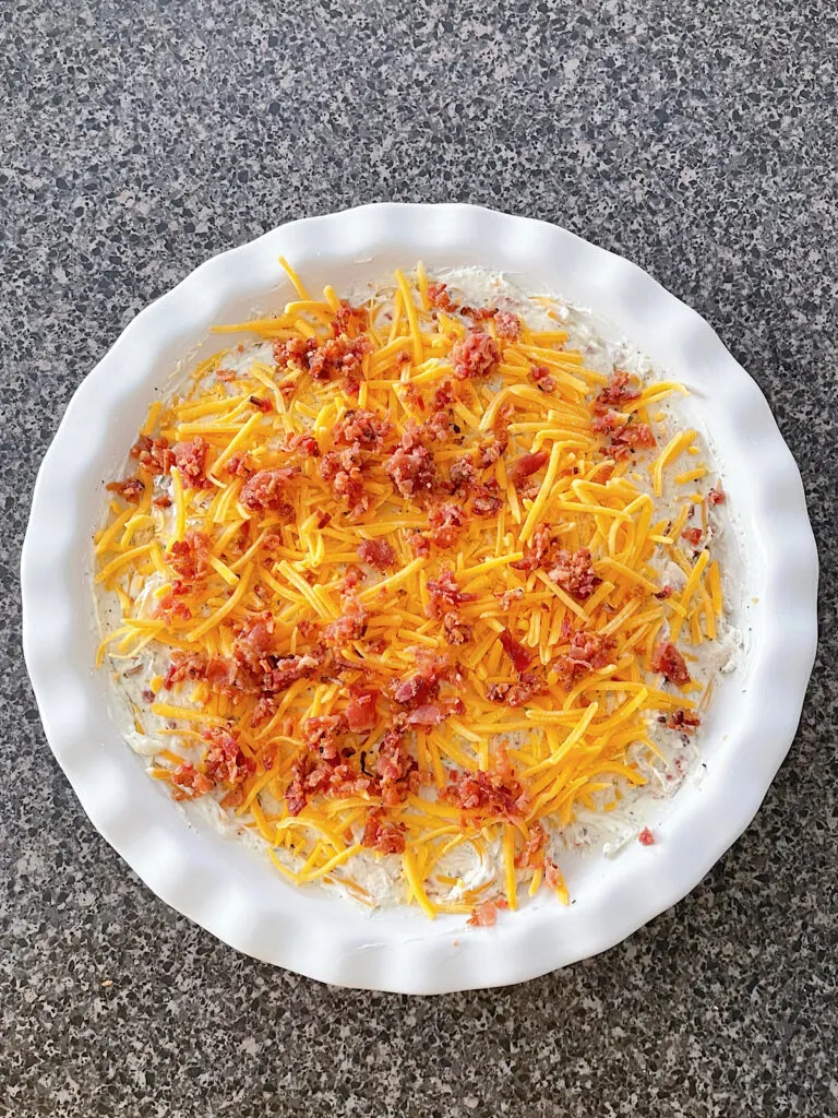 Cream cheese chicken dip topped with bacon and cheese in a baking dish.