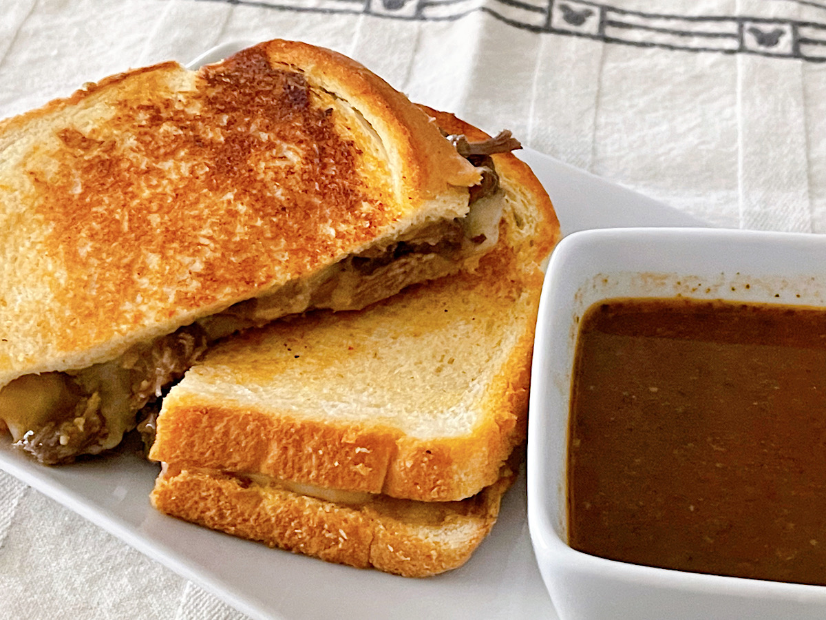 A copycat Disneyland beef birria grilled cheese with a side of consommé.