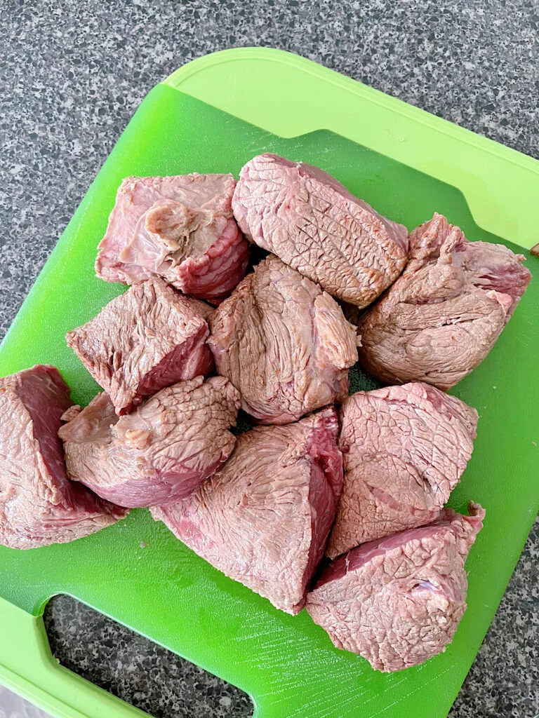Chuck roast that has been seared and cut into chunks on a green cutting board.