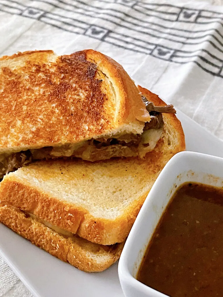 A copycat Disneyland beef birria grilled cheese with a side of consommé.