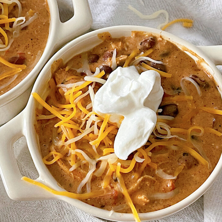 Two bowls of Cream Cheese Chicken Chili topped with shredded cheese and sour cream.