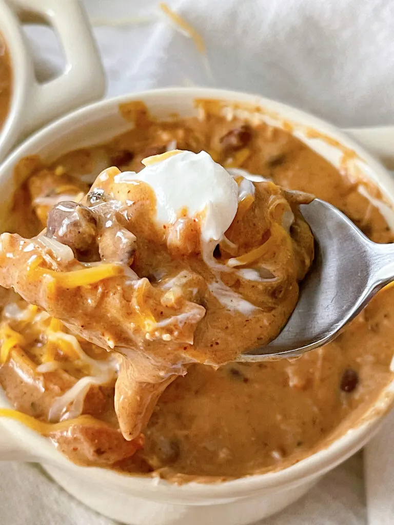 Cream Cheese Chicken Chili in a bowl topped with sour cream and shredded cheese.