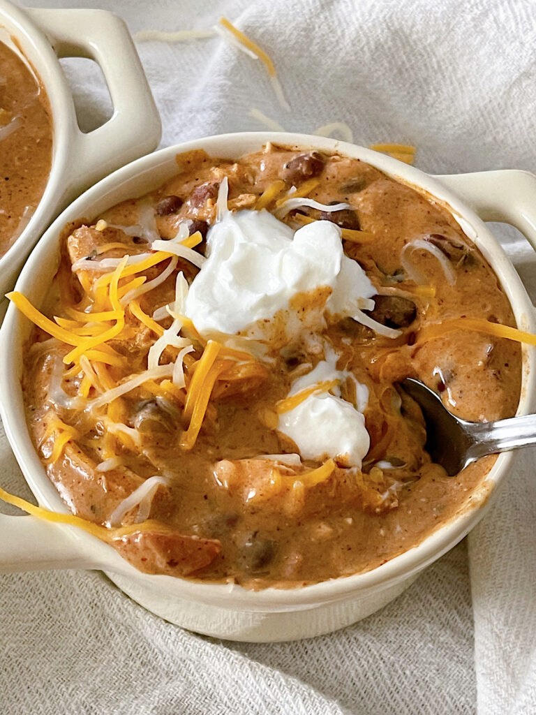 Cream Cheese Chicken Chili in a bowl topped with sour cream and shredded cheese.
