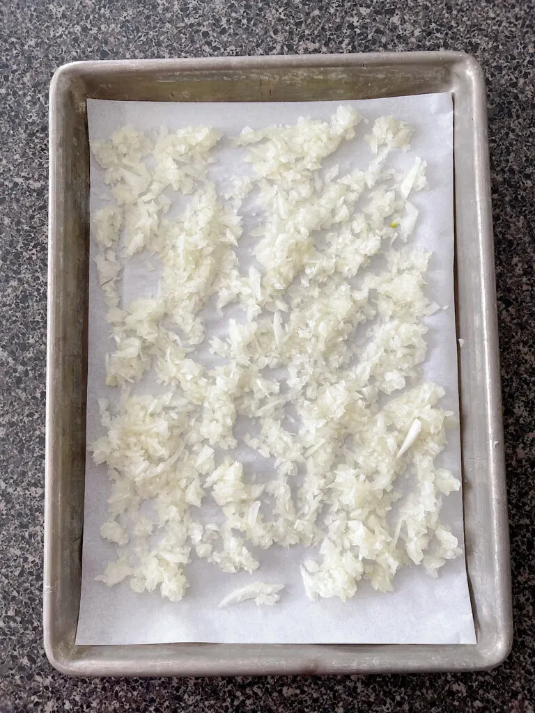Chopped onions on a parchment paper lined baking sheet.