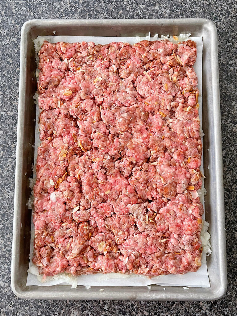A large hamburger patty on a parchment paper lined baking sheet.