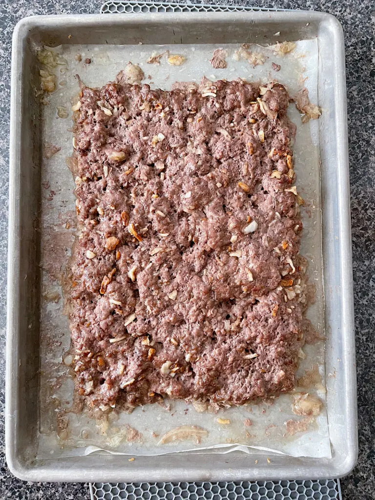 A large cooked hamburger patty on a parchment paper lined baking sheet.