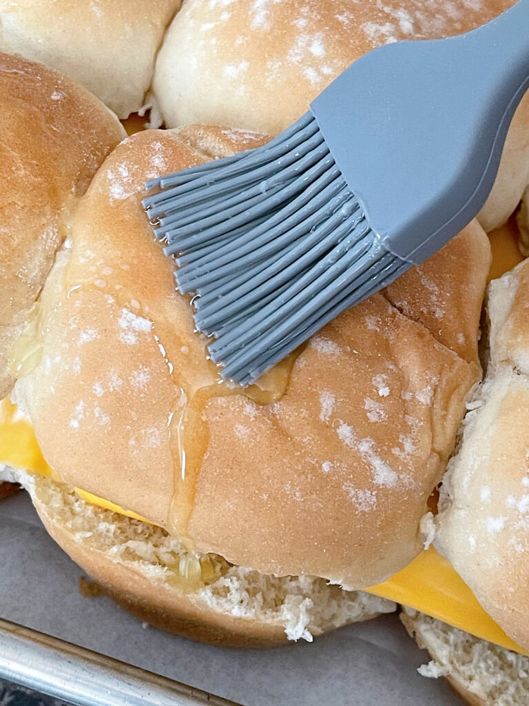 Brushing melted butter on top of slider buns.