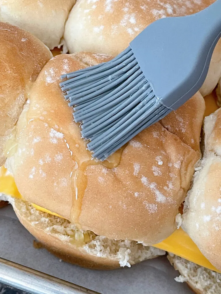 Brushing melted butter on top of slider buns.