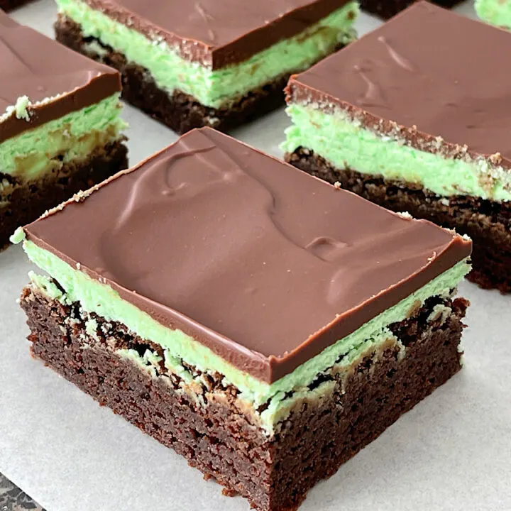 Brownies topped with mint frosting and chocolate ganache on a piece of parchment paper.