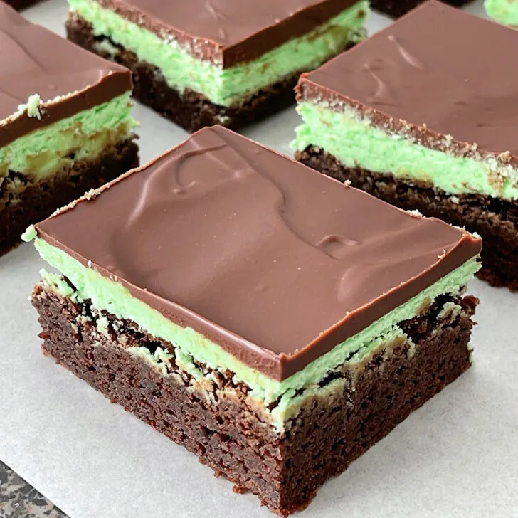Brownies topped with mint frosting and chocolate ganache on a piece of parchment paper.