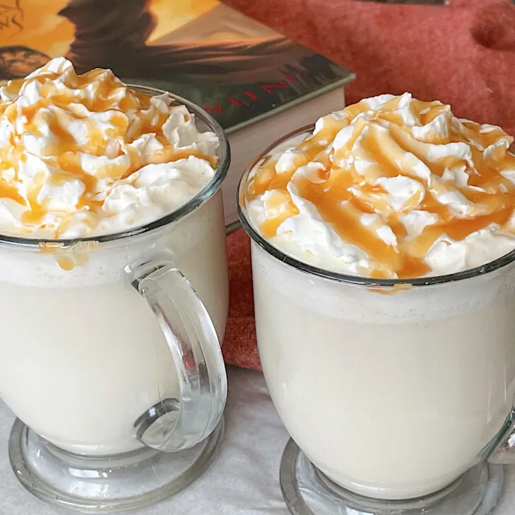 Two mugs of hot butterbeer topped with whipped cream and caramel.