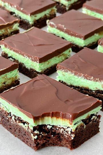 Brownies topped with mint frosting and chocolate ganache on a piece of parchment paper.