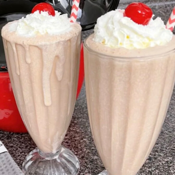 Two chocolate malts topped with whipped cream and a cherry.