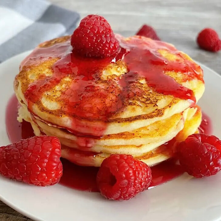 A stack of lemon ricotta pancakes with raspberry syrup.