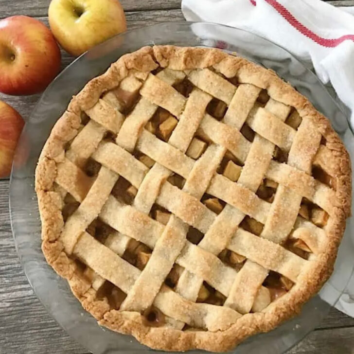 A caramel apple pie with three apples and akitchen towle.