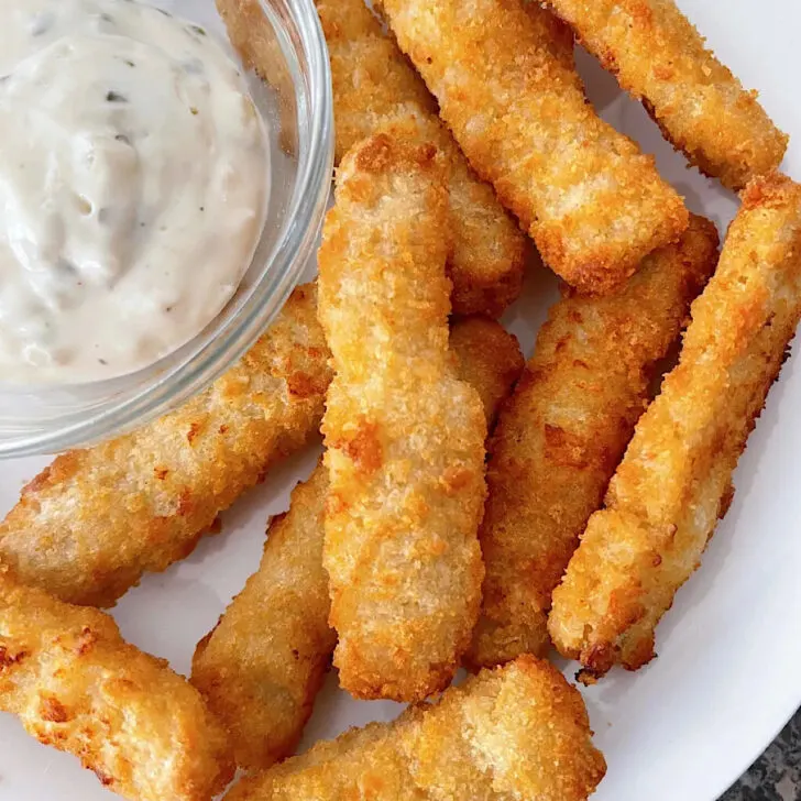 Fish sticks on a plate with a bowl of tartar sauce.