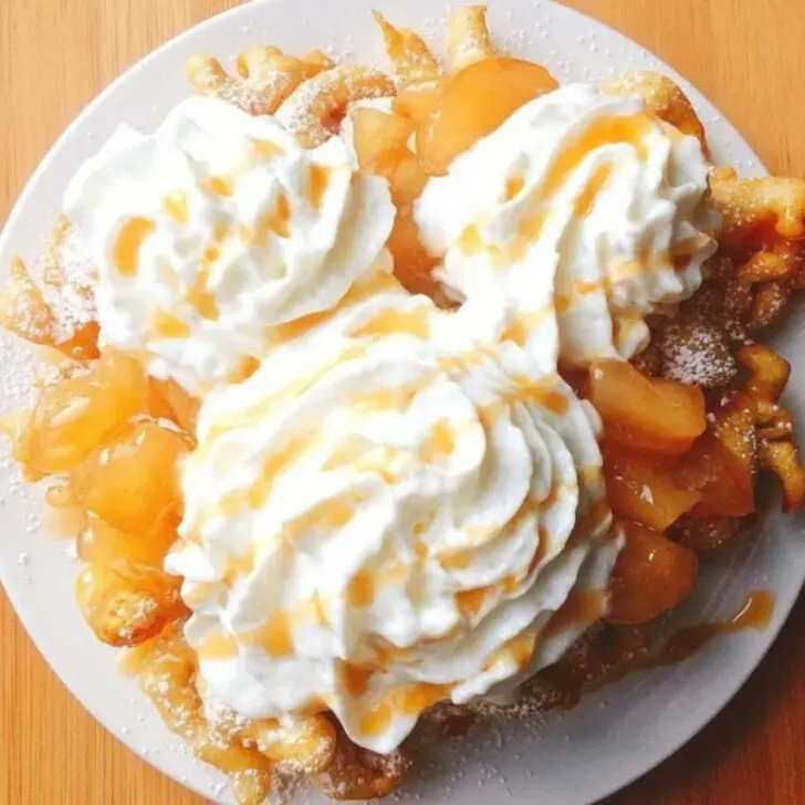 A funnel cake topped with apple pie filling and Mickey Mouse-shaped whipped cream.
