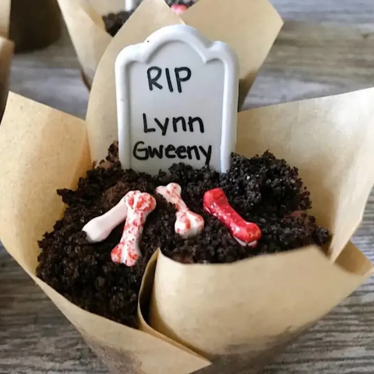 A cupcake topped with OREO cookie crumbs, candy bones, and a candy headstone.