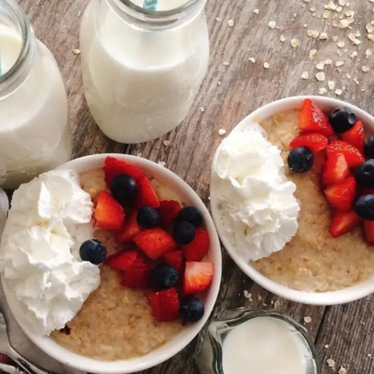 Two bowls of oatmeal with berries and whipped cream.